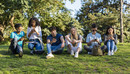 Group of teenage friends looking at phone in the park on green grass. Three boys and three girls