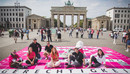 Junge Menschen sitzen vor dem Brandenburger Tor in Berlin auf einem überdimensionierten Scrabble-Spielfeld, auf dem das Wort Gerechtigkeit steht