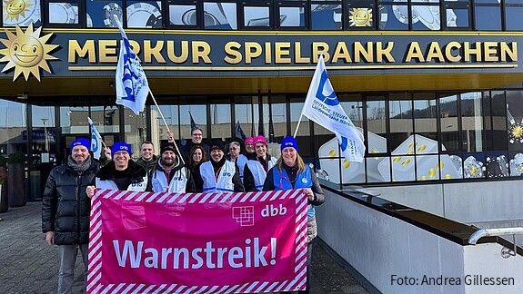 Eine Gruppe Menschen demonstriert vor einem großen Gebäude mit der Aufschrift "Merkur Spielbank Aachen"