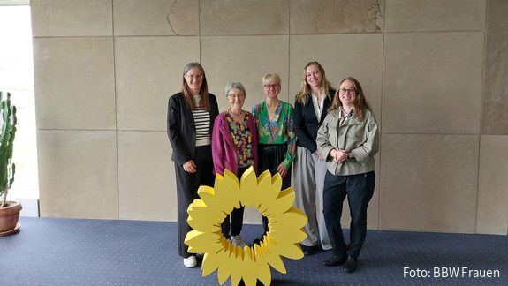 Fünf Frauen stehen hinter einem gelben Aufsteller im Design einer großen gelben Blüte