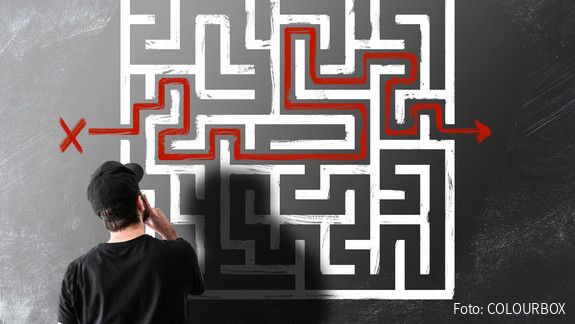Junger Mensch steht vor einem an die Wand gezeichneten Labyrinth und denkt nach.