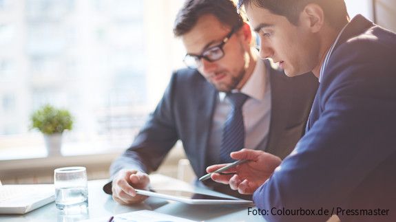 Zwei Männer im Büro sehen gemeinsam auf Tablet und besprechen sich