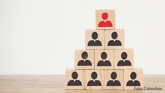 Das Foto zeigt Würfel, die als Pyramide gestapelt sind. Auf den Würfeln jeweils Figuren, die oberste ist rot. 