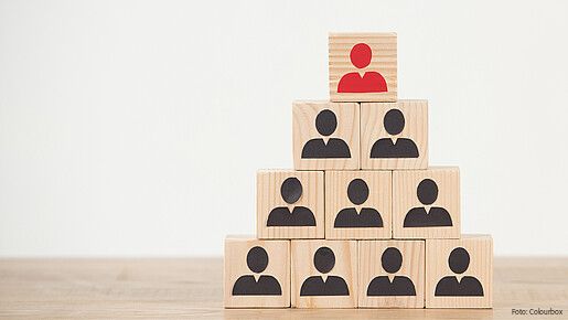 Das Foto zeigt Würfel, die als Pyramide gestapelt sind. Auf den Würfeln jeweils Figuren, die oberste ist rot. 