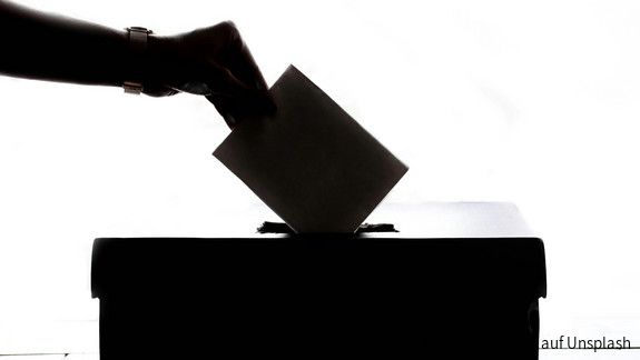 Ein Wahlschein wird in die Wahlurne eingeworfen