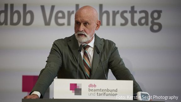 Ein Mann in Anzug steht hinter einem Rednerpult und spricht in ein Mikrofon