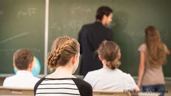 Streit um Unterbringung von Berufsschule Das Foto zeigt einen Lehrer, der etwas an die Tafel schreibt, im Vordergrund sind die Hinterköpfe von Schülerinnen und Schülern zu sehen.