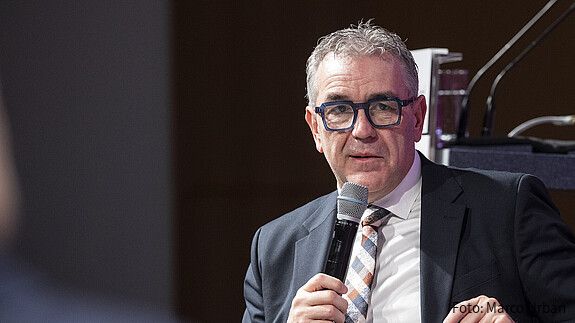 Ein Mann sitzt in einer Diskussionsrunde und spricht in ein Mikrofon