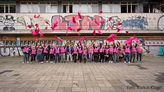Junge Beschäftigte des öffentlichen Dienstes vor einem leerstehenden, heruntergekommenen Gebäude
