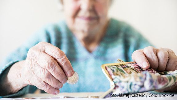Eine unglücklich wirkende Seniorin zählt am Tisch die wenigen Münzen ihre Pension.