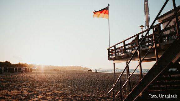 An einen Stelzenhaus am Strand ist die Deutschlandflagge gehisst, im Hintergrund scheint die Abendsonne. 