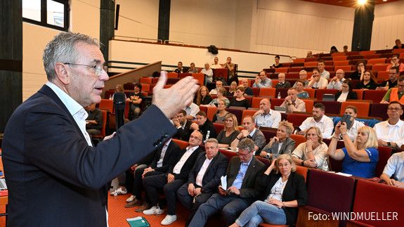 Ein Mann im Anzug spricht vor Anwesenden in einem Hörsaal