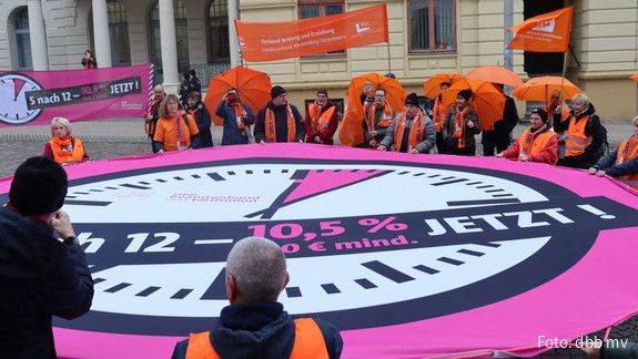 Es ist 5 nach 12 - Flashmob in Schwerin Demonstranten haben ein pinkes Banner in Form einer Uhr aufgespannt, auf dem "es ist 5 nach 12" geschrieben steht.