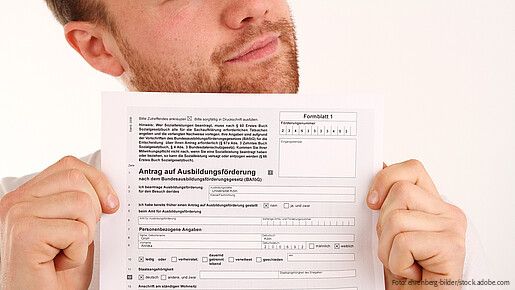 Person hält ein BAföG-Antragsformular mit der Überschrift „Antrag auf Ausbildungsförderung“ in die Kamera.