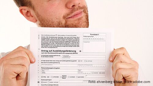 Person hält ein BAföG-Antragsformular mit der Überschrift „Antrag auf Ausbildungsförderung“ in die Kamera.